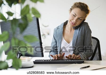 Stock Image - Young businesswoman working on desktop computer in office. Fotosearch