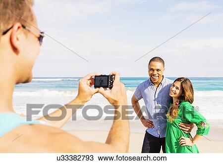 Young man taking photo of couple on beach View Large Photo Image Stock Image - Young man taking photo of couple on beach. Fotosearch