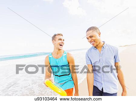 Picture - Young man walking and talking, holding plastic disc on beach. Fotosearch