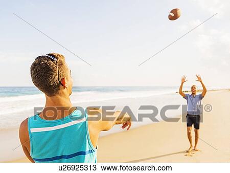 Stock Image - Young men playing football on beach . Fotosearch