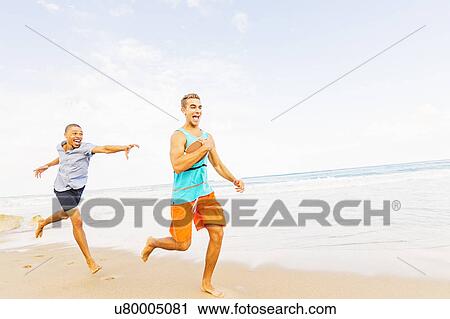 Stock Image - Young men playing with football on beach . Fotosearch