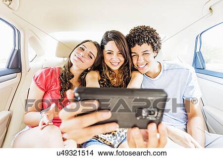 Picture - Young people and teenager (14-15) taking selfie in car. Fotosearch