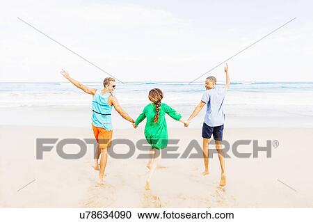 Stock Image - Young people holding hands and running on beach. Fotosearch