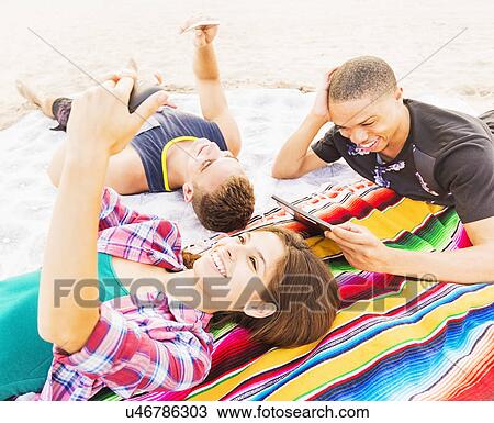 Young people lying on blanket, using technology View Large Photo Image Stock Image - Young people lying on blanket, using technology. Fotosearch