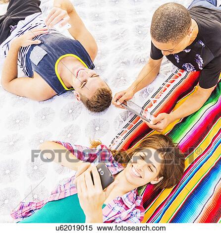 Young people lying on blanket, using technology View Large Photo Image Stock Photography - Young people lying on blanket, using technology. Fotosearch