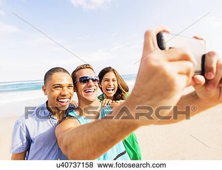 Stock Photo - Young people taking selfie on beach. Fotosearch