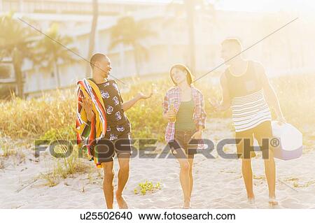 Stock Image - Young people walking on beach at sunset. Fotosearch