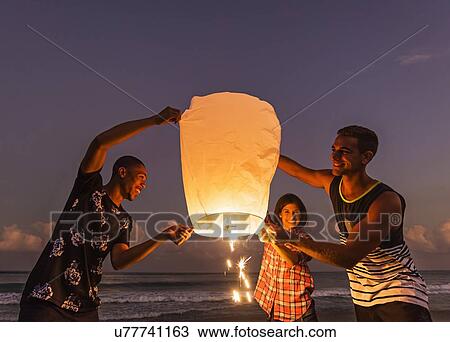 Stock Image - Young people with illuminated lantern on beach. Fotosearch