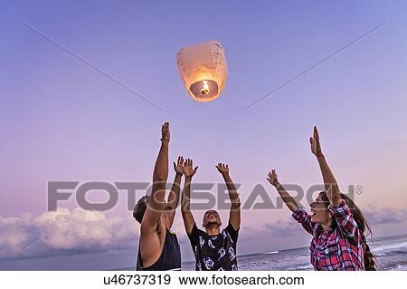 Stock Photo - Young people with illuminated lantern on beach. Fotosearch