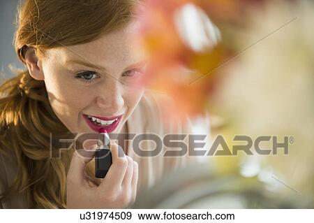 Stock Photo - Young woman applying lipstick. Fotosearch
