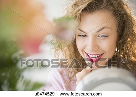 Young woman applying red lipstick in front of mirror View Large Photo Image Stock Image - Young woman applying red lipstick in front of mirror. Fotosearch