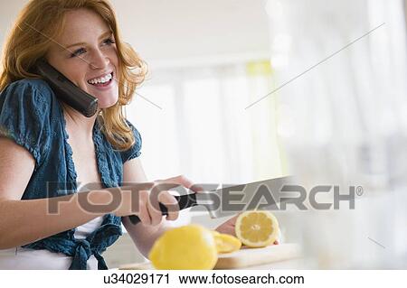 Stock Image - Young woman cutting lemon and talking on phone. Fotosearch