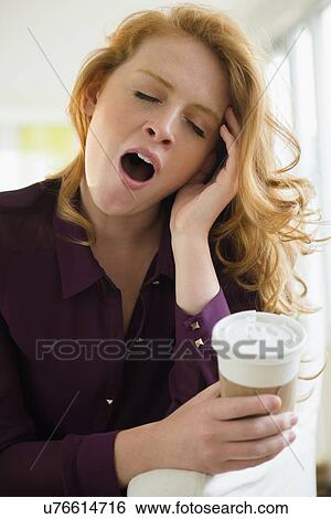Stock Photograph - Young woman holding disposable cup and yawning. Fotosearch
