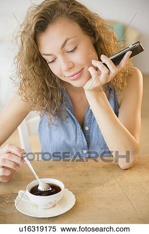 Young woman holding smart phone and stirring tea View Large Photo Image Stock Photography - Young woman holding smart phone and stirring tea. Fotosearch