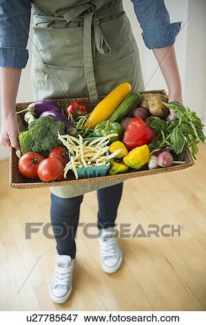 Stock Photo - Young woman holding tray with vegetables. Fotosearch