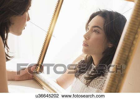 Stock Image - Young woman looking into mirror. Fotosearch