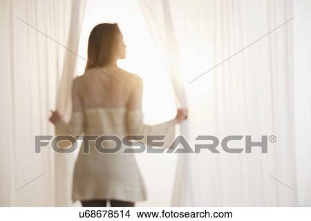 Picture - Young woman opening curtains in morning. Fotosearch