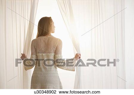 Young woman opening curtains in morning View Large Photo Image Stock Image - Young woman opening curtains in morning. Fotosearch
