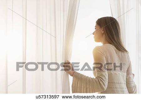 Young woman opening curtains in morning View Large Photo Image Stock Photo - Young woman opening curtains in morning. Fotosearch