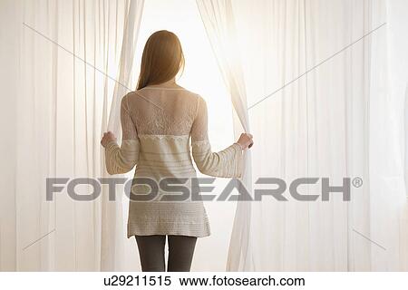 Stock Photography - Young woman opening curtains in morning. Fotosearch