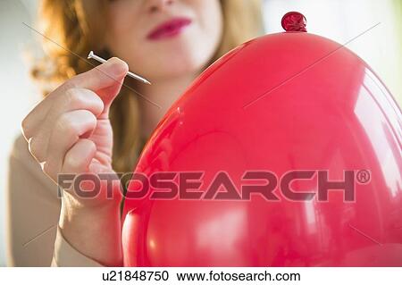 Stock Image - Young woman popping balloon. Fotosearch