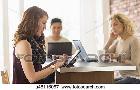 Stock Photo - Young woman sitting in cafe and using digital tablet. Fotosearch