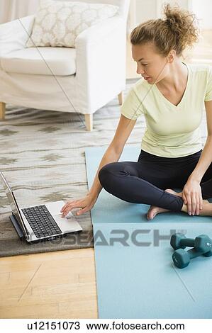 Young woman sitting on yoga mat and using laptop in living room View Large Photo Image Stock Image - Young woman sitting on yoga mat and using laptop in living room. Fotosearch