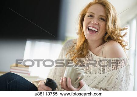 Stock Photography - Young woman watching television and laughing. Fotosearch