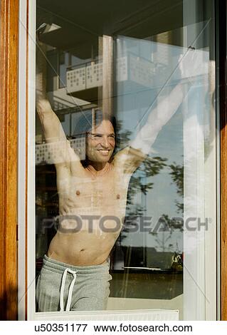 Bare-chested man stretching at window View Large Photo Image Stock Photo - Bare-chested man stretching at window. Fotosearch
