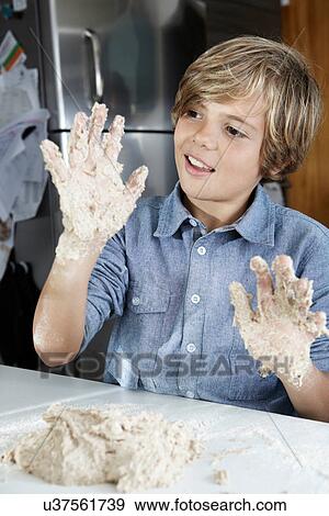 Stock Photo - Boy examining sticky hands in kitchen. Fotosearch