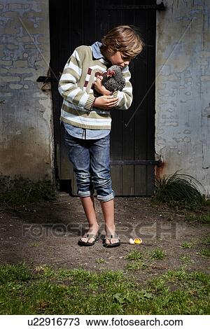 Stock Image - Boy holding chicken outdoors. Fotosearch