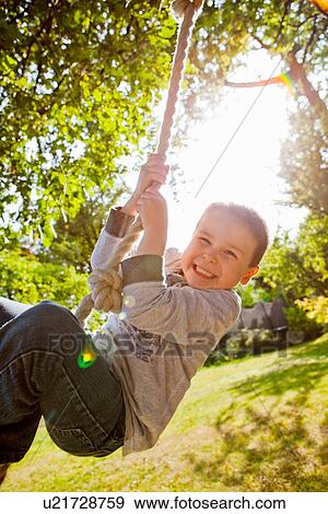 Boy playing on rope swing in backyard View Large Photo Image Stock Photo - Boy playing on rope swing in backyard. Fotosearch