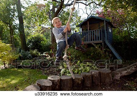 Stock Photography - Boy playing on rope swing in backyard. Fotosearch