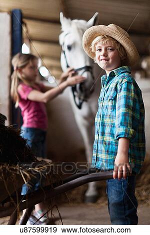 Stock Photo - Boy pushing wheelbarrow in stable. Fotosearch