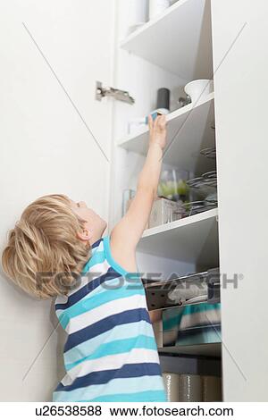Stock Photo - Boy reading for something in cabinet. Fotosearch