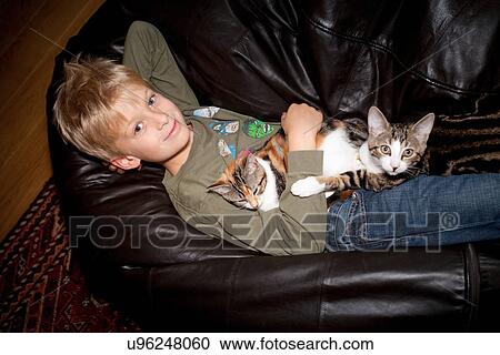 Stock Image - Boy relaxing with cat on couch. Fotosearch