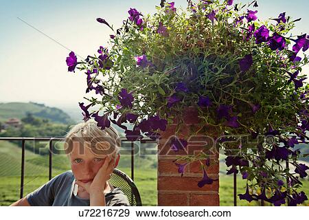 Stock Photo - Boy sitting by potted plant outdoors. Fotosearch