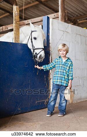 Stock Image - Boy standing with horse in stable. Fotosearch