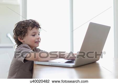 Stock Image - Boy using laptop at desk. Fotosearch