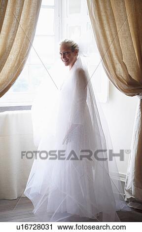 Bride wearing long veil in window View Large Photo Image Stock Image - Bride wearing long veil in window. Fotosearch