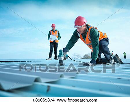 Building foreman reading plans as workman insulates factory roof View Large Photo Image Picture - Building foreman reading plans as workman insulates factory roof. Fotosearch
