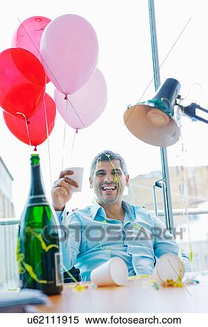 Stock Photography - Businessman at desk during office party. Fotosearch