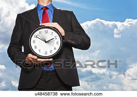 Businessman holding backwards clock View Large Photo Image Stock Photo - Businessman holding backwards clock. Fotosearch
