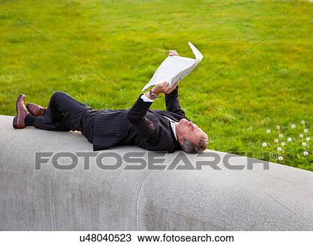 Stock Image - Businessman reading newspaper in park. Fotosearch