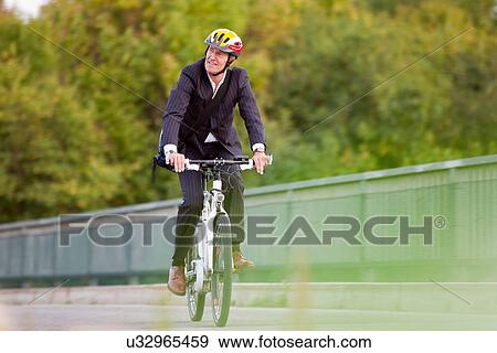Stock Photo - Businessman riding bicycle on bridge. Fotosearch