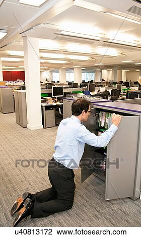Stock Image - Businessman searching in file cabinet. Fotosearch