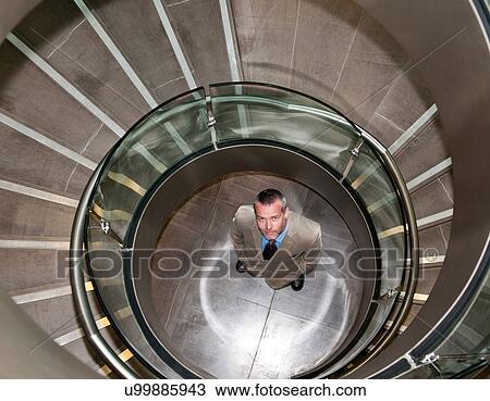 Stock Image - Businessman standing in spiral staircase. Fotosearch