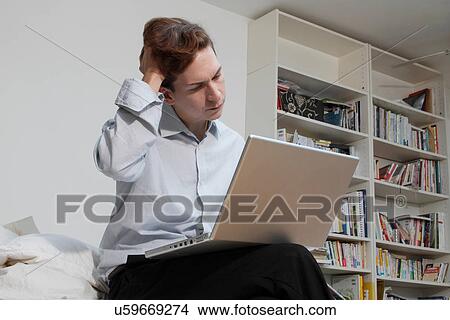 Picture - Businessman using laptop in bedroom. Fotosearch
