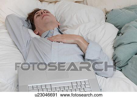 Stock Image - Businessman with laptop laying on bed. Fotosearch