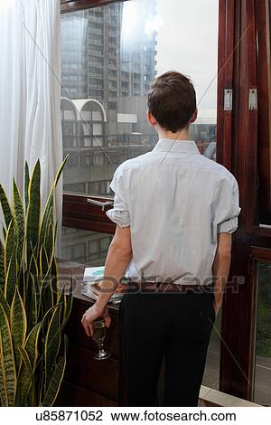 Stock Image - Businessman with wine looking out window. Fotosearch